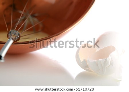 a beautiful copper mixing bowl with a whisk and beaten eggs and egg shells on white with nice reflections