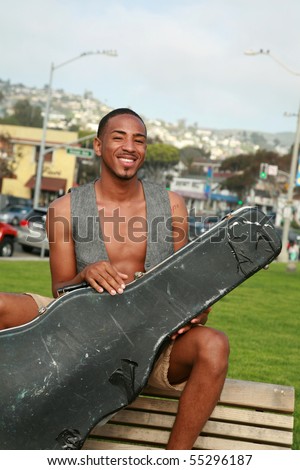 a young man poses with his old worn out guitar case outside in a park