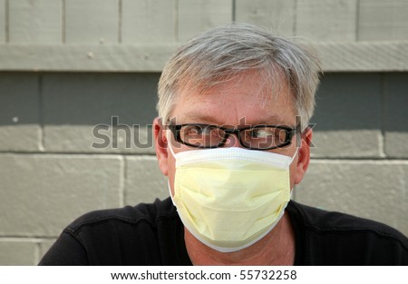 a man wears a yellow medical paper mask as he looks around to stay safe from any air born illness