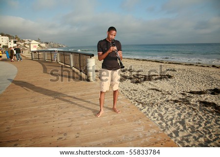 a young man plays his clarinet outside at the beach for all to hear and enjoy