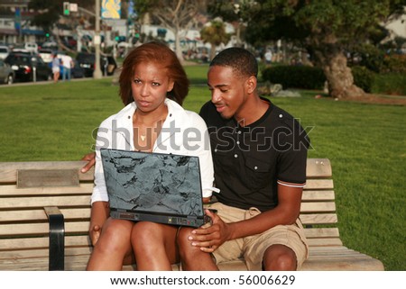 a young couple use a laptop computer outside in a park