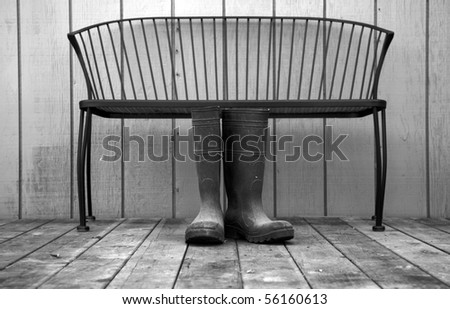 rubber boots sit on a wooden porch next to a bench in black and white