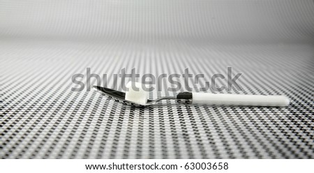 a pure white sugar cube on a silver spoon with a white plastic handle on a black and white background