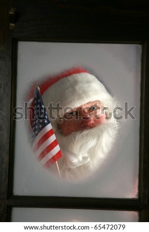 Santa Claus looks out through the snow and fog on his workshop window in the north pole to see outside check the weather while he holds up an American Flag on December 24th, Christmas Eve