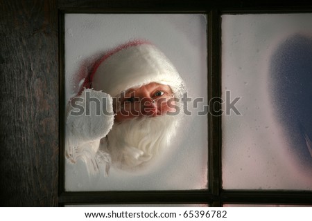 Santa Claus wipes the snow and fog away from his workshop window in the north pole to see outside and make sure his raindeer are getting ready to go to work on December 24th, Christmas Eve