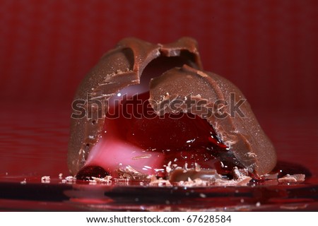 Chocolate covered cherry that has a bite taken out of it, so its juice flows out against a red and white pokadot background perfect for valentines day images