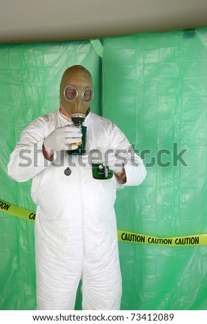 A Nuclear Scientist or Chemical Engineer wears a white Hazmat Suit, Gas Mask, and Gloves as he mixes dangerous chemicals together while in a temperary plastic wrapped \