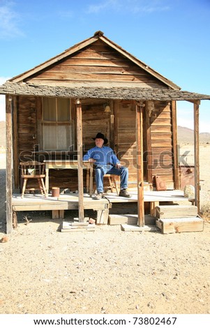 an old cowboy sits on the porch of his home after a hard day of ropin and riding the range