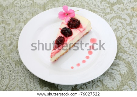 raspberry cheesecake with rasberries, raspberry sauce, a pink flower, and a fork on a green table cloth and napkin. just waiting for you to enjoy as your dessert after dinner or anytime you like