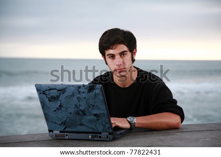 a young man does his school work, or surfs the web on his laptop computer while at the beach. He could be on Spring Break or Summer Vacation or even Skipping School or on the Weekend. You decide