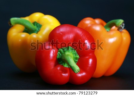 beautiful yellow, orange, and red. bell peppers with green stems on a black background in a \