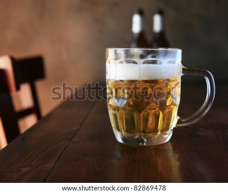 Beer. What more can I say?  Fresh been in a mug on a wooden table with a nice dark wall as a background in a restaurant on hot summer day.