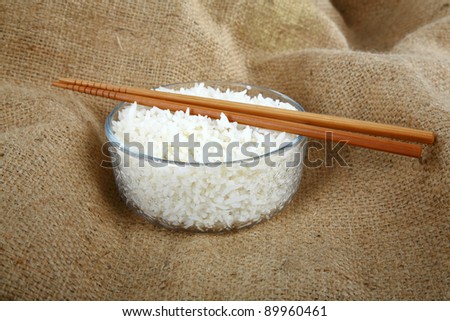 a bowl of steamed white rice on burlap with bamboo chop sticks