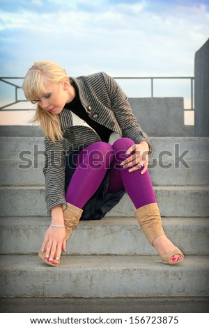 Blond young girl sits on stair on background blue sky with clouds