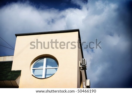 Fragment of the house with round window on background blue sky with clouds