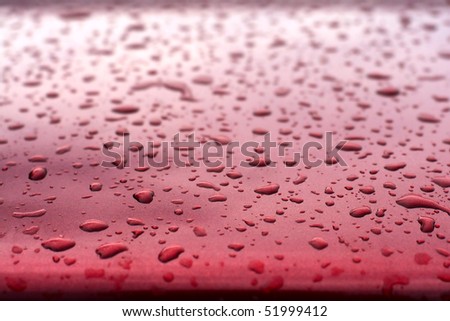 Surface of my red car after rain. Water drops collect on top of metal surface.