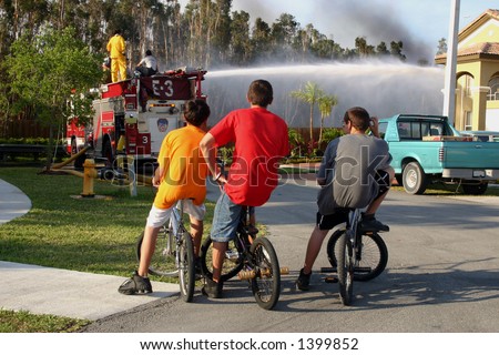 3 teens observing firemen put out a fire. Brand Names & Logos removed.