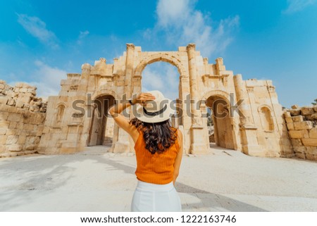 Asian young woman tourist in color dress and hat leading man to South gate of the Ancient Roman city of Gerasa, modern Jerash, Jordan. Traveling together. Follow me.