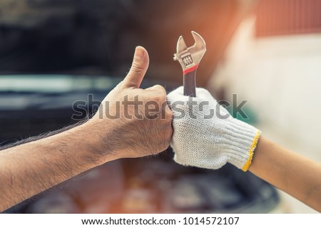 Mechanic hand checking and fixing a broken car in  garage.hand of mechanic with thumbs up and tool