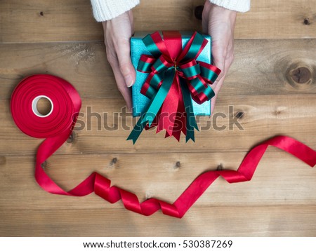 Creative hobby. Woman\'s hands wrap christmas holiday handmade present in craft paper with twine ribbon. Making bow gift box, decorated with cute object on wooden table, top view.flat lay composition
