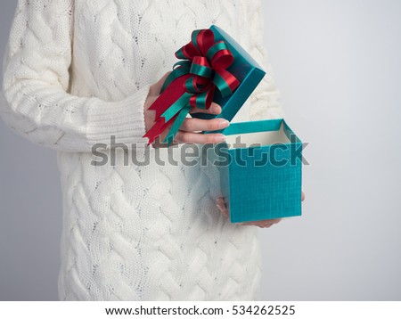 Close up shot of female hands holding and open gift box and nice ribbon. Gift box color in the hands of a woman wearing a knitted hat sweater on white background.