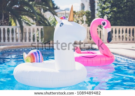 Inflatable colorful white unicorn and pink flamingo at the swim pool. Vacation time in the swimming pool with plastic toys. Relaxation and fun concept