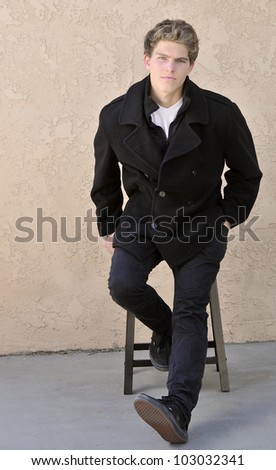 Portrait of an Attractive Young Male Model Sitting on a Stool with a P Coat