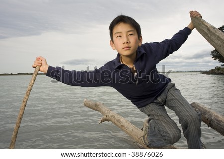 11 year old Asian boy balancing on log in water