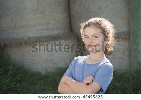 little girl (7 years old) standing in front of a background of bales of hay on a New Zealand farm
