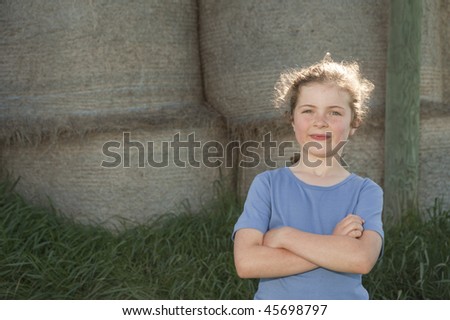 little girl (7 years old) standing in front of a background of bales of hay on a New Zealand farm