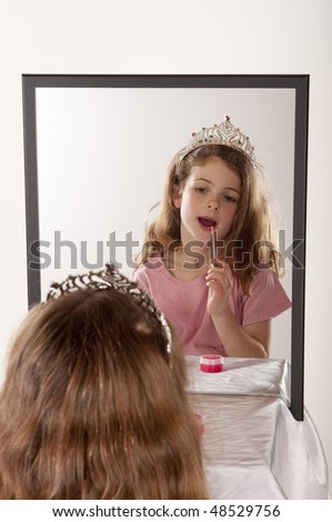 little girl looking at herself in mirror while playing lip gloss and fairy princess