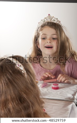 little girl looking at herself in mirror while playing lip gloss and fairy princess
