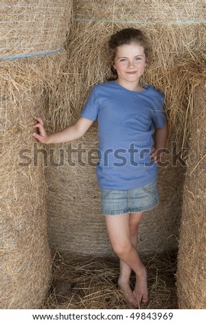 little girl (7 years old) standing amongst bales of hay in a barn MR