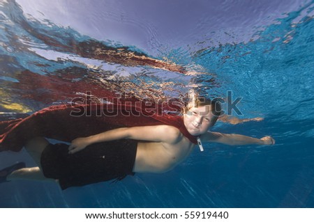 8 year old boy wearing towel for cape and pretending to fly underwater  MR