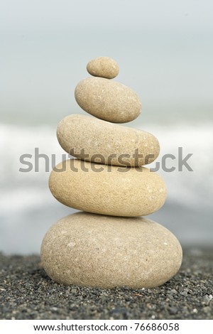 pile of balanced rocks on black sand beach against ocean background