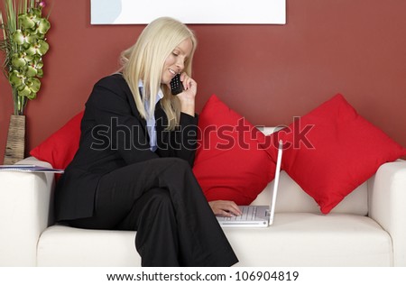 Young woman sitting on a sofa chatting on the phone and working