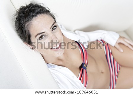 Beautiful young woman in white open shirt and red bikini resting on her sofa at home