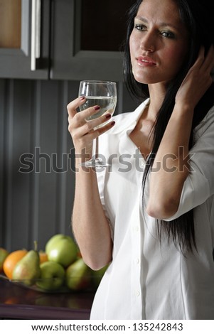 Attractive young woman enjoying a glass of wine in her kitchen.