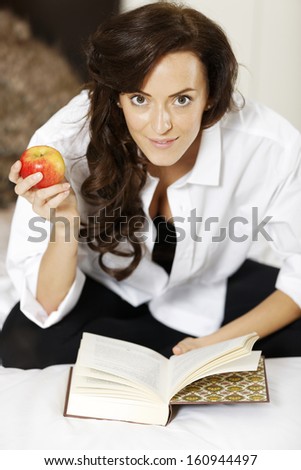 Attractive young woman enjoying a good book in bed.