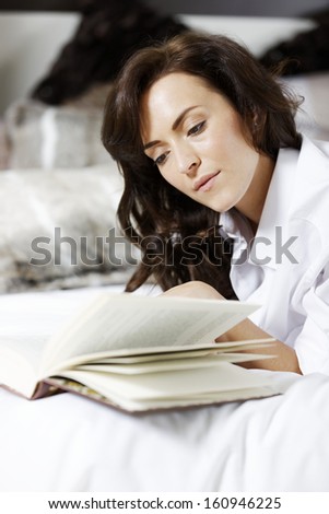 Attractive young woman enjoying a good book in bed.