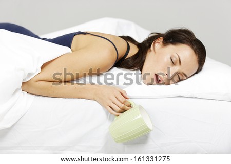 Young woman falling asleep in bed with drink in hand