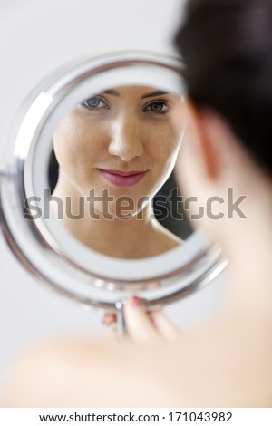 Attractive young woman looking into a make up mirror