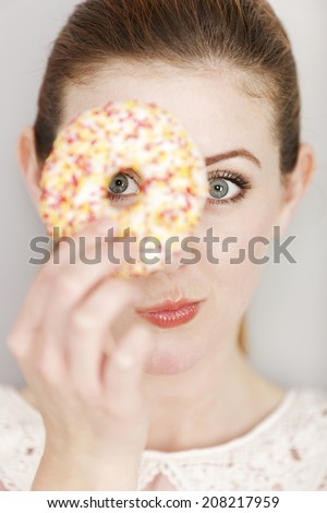 Young woman holding a ring doughnut over her eye smiling.