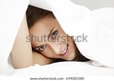 Young woman peeking through her bed sheets
