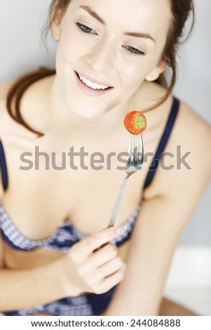 Attractive young woman holding up a strawberry wearing her underwear