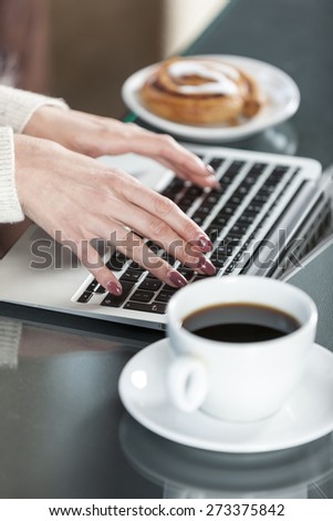 Woman's hands typing on a laptop keyboard with coffee and fresh cake