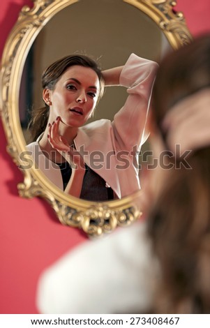 Attractive young woman fixing her hair in the mirror before work