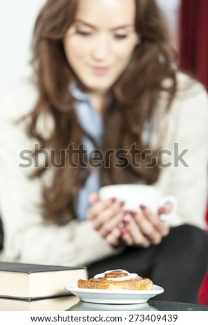 Beautiful young woman enjoying a fresh cup of coffee in a coffee shop with a book and a cake