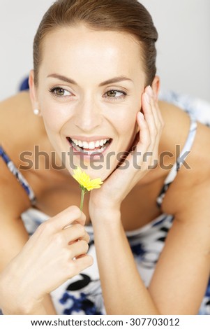 Beautiful young woman holding a single fresh yellow flower smiling
