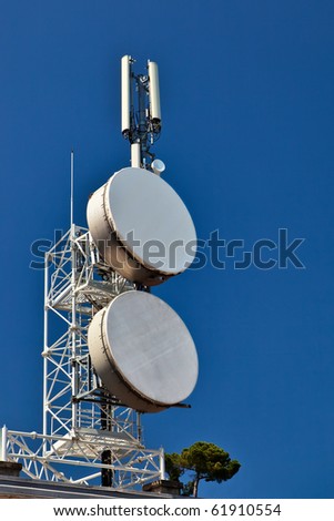Telecommunication mast with microwave links and cellular network antennas over a blue sky.